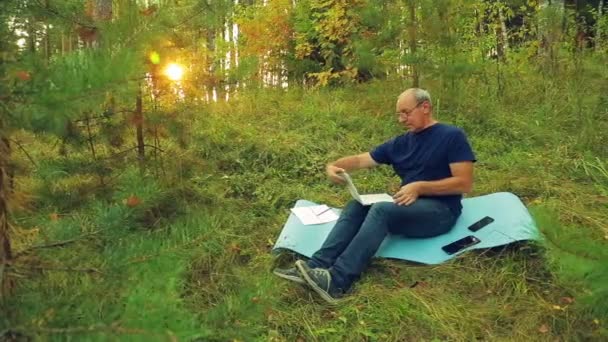 En man med glasögon i en skog glade arbetar med en bärbar dator. — Stockvideo