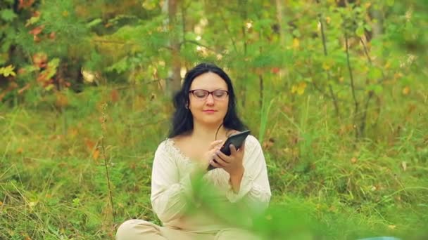 Genç bir kadın ormandaki bardaklarda çimenlerin üzerinde oturur ve bir Messenger'da iletişim kurar. — Stok video