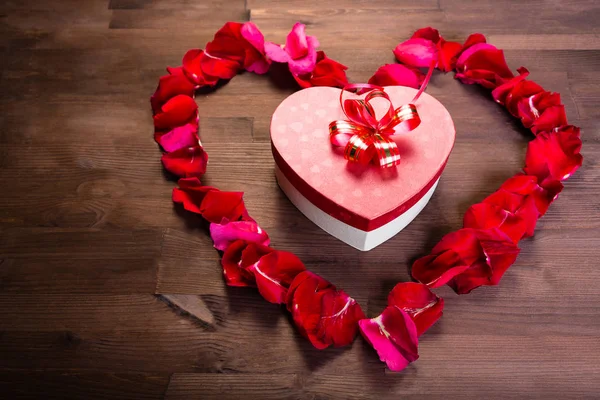 Ahşap masanın üstüne gül lepistas kalp içinde bir hediye bir kalp şeklinde bir kutudur. Orta planı
