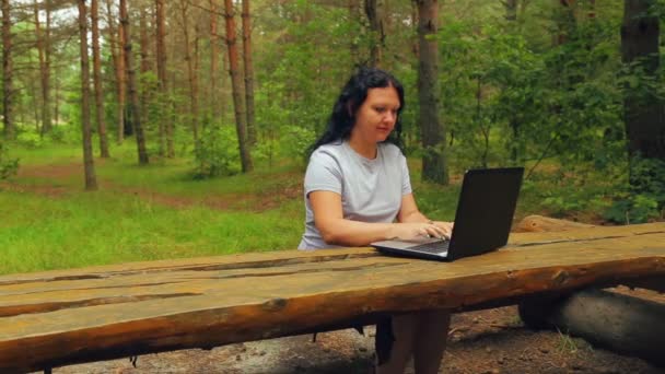 Mujer joven en un parque escribiendo en un ordenador portátil . — Vídeos de Stock