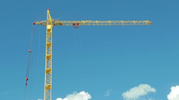 Een gebouw toren kraan zwaait de wind, tegen een blauwe hemel met bewegende witte wolken. Tijd ronden — Stockvideo