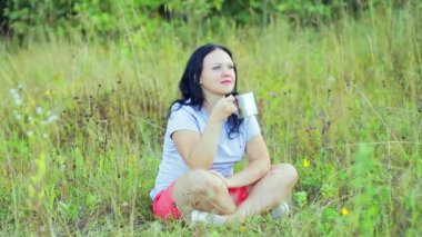 çay içme ve doğa hayran bir açıklıkta çimenlerin üzerinde oturan genç mutlu kadın.