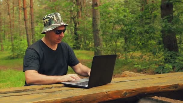 Man in sunglasses typing on laptop keyboard in park — Stock Video