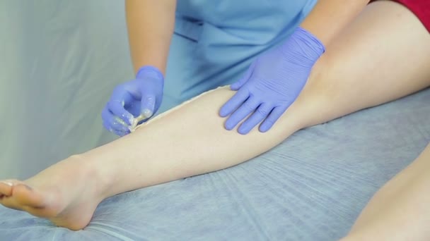Um cosmetician fêmea aplica a pasta de açúcar na pele das pernas dos clientes . — Vídeo de Stock