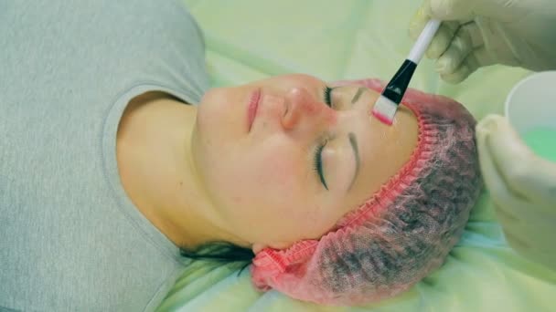 Руки чоловіка косметолога одягнули на обличчя жінки рідку маску за допомогою пензлика — стокове відео