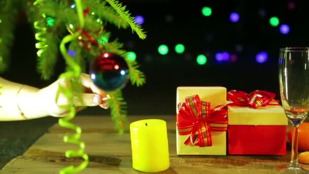 Женщина зажигает свечу, которая находится рядом с рождественскими подарками на столе рядом с елкой и мандарины на черном фоне с огнями — стоковое видео