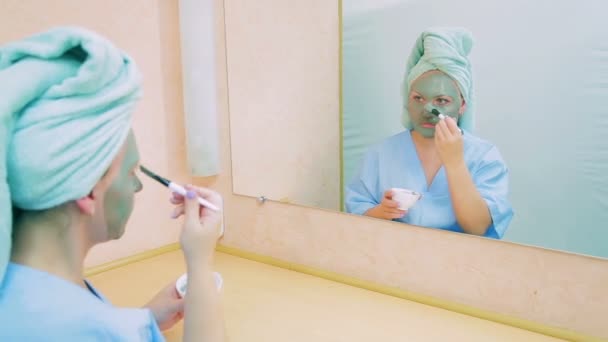 Een jonge actrice in een make-up kamer voor een spiegel zet een masker op haar gezicht met een borstel. — Stockvideo