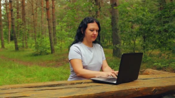 Молода жінка в парку друкує на ноутбуці — стокове відео