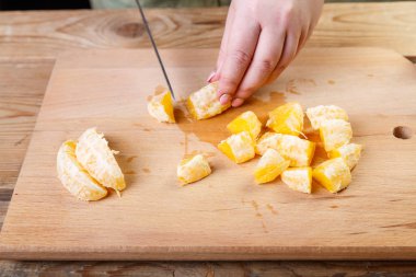 Bir kadın bir portakal ahşap kesme tahtası üzerinde onu bıçakla keser