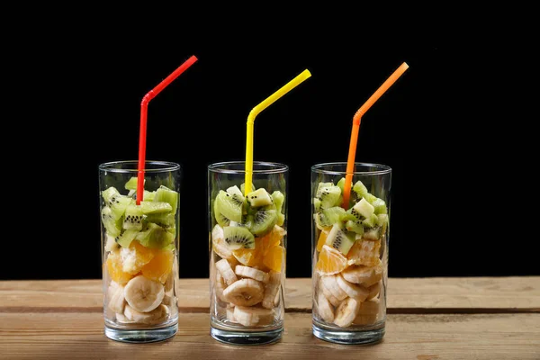 ahşap bir masaya üç bardak meyve ve meyve kokteyli için tüpler vardır