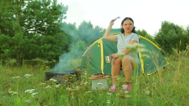 Een jonge vrouw met zonnebril zit in de buurt van de grill en thee drinken. — Stockvideo