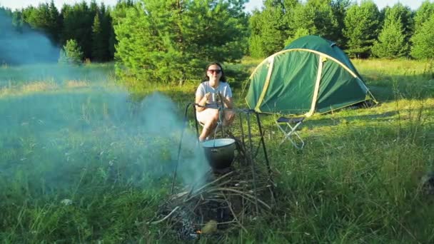 Un homme et une femme sont assis près du feu de camp près de la tente et boivent du thé — Video