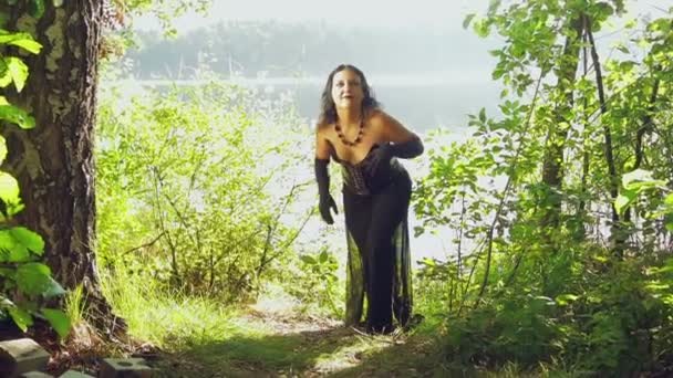 Une femme est une sorcière vêtue de noir sur la rive d'un lac. Halloween. Style gothick — Video