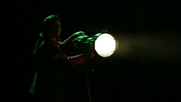 Una mujer iluminadora dirige un haz de luz desde un reflector de perfil — Vídeos de Stock