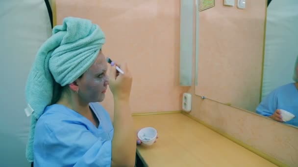 An actress in a dressing room at a table in front of a mirror applies a nourishing mask on her face with a brush. Profile — Stock Video