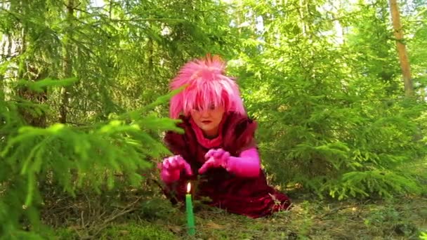 Молодая ведьма над горящей свечой, стоящей на земле в лесу, читает заклинание — стоковое видео