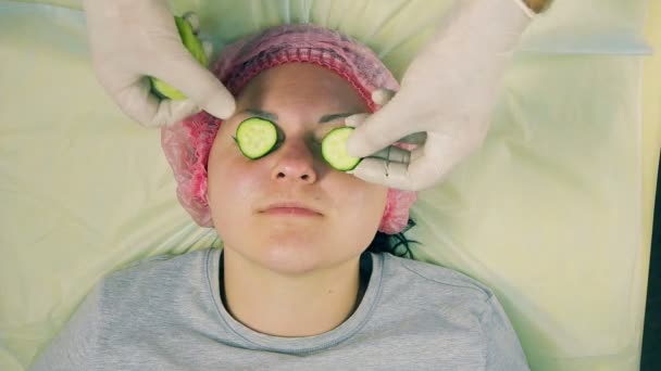 Руки чоловіка-косметолога в рукавичках накладають маску ківі і огірка на обличчя жінки — стокове відео