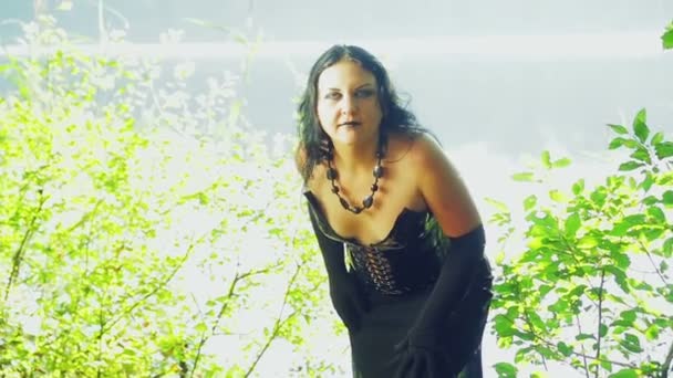Une femme d'une sorcière en vêtements noirs sur la rive du lac regarde autour. Halloween. Style gothick . — Video