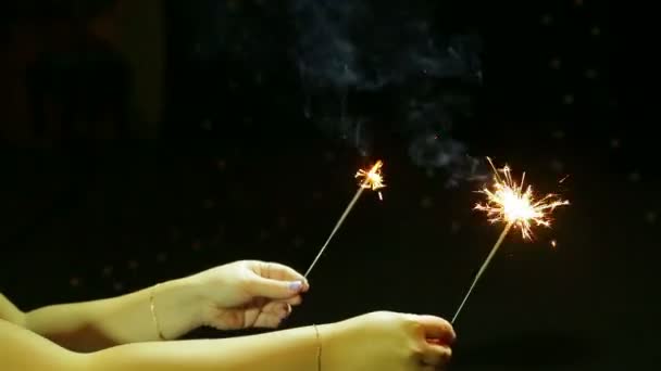 Un hombre y una mujer celebran la Navidad de Año Nuevo con fuegos artificiales de vela de Bengala sobre un fondo negro . — Vídeo de stock