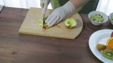 Bir kadın bir elma bir ahşap tahta üzerinde dilimler halinde bıçakla keser. Kamera sağdan sola taşır.