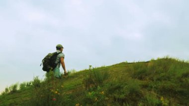 Sırtında bir sırt çantası ile kadın turist yeşil bitki örtüsü ile kaplı bir dağ yükselir.