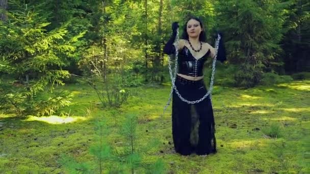 Une jeune sorcière en vêtements noirs libérés des chaînes tourne avec eux dans la forêt. Halloween. Style gothick — Video