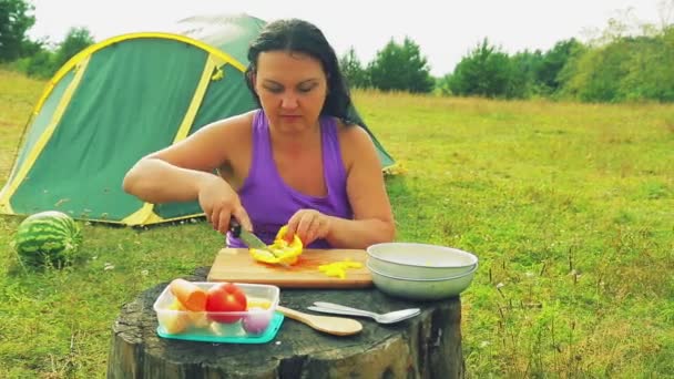 Una donna vicino a una tenda scivola peperoni gialli su piccoli cubetti con un coltello su una tavola di legno . — Video Stock