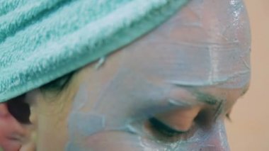 Kafasındaki bir havlu ile gülümseyen kadın yüz derisinin üzerinde mavi kil bir fırçayla.