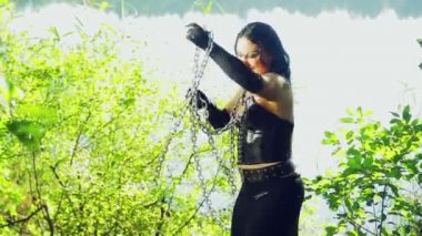 göl kıyısında siyah giysili bir kadın cadı zincirleri elinde eğleniyor. Cadılar Bayramı. Gothick tarzı