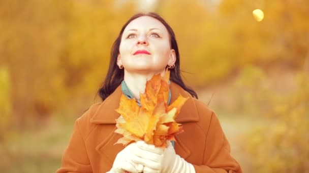 Eine junge Frau im Herbst im Park mit einem Strauß Ahornblättern in der Hand bewundert die Natur. Zeitlupe. — Stockvideo