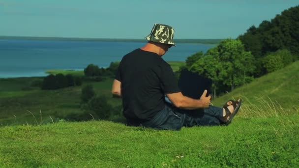 Žena sedí na kopci s výhledem na jezero a otevření krytu přenosného počítače — Stock video
