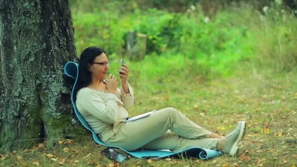 The girl sits in a park under a tree and is painted with lipstick. Close-up. — Stock Video