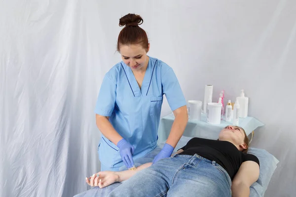 Een vrouwelijke arts schoonheidsspecialiste maakt een shugaring liggend op een dames massagetafel door een patiënt op haar rechterarm. — Stockfoto