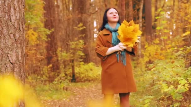 Sonbahar parkta bir yürüyüş önlüğünü genç bir kadın onun elinde akçaağaç yaprakları hayran. Ağır çekim. — Stok video