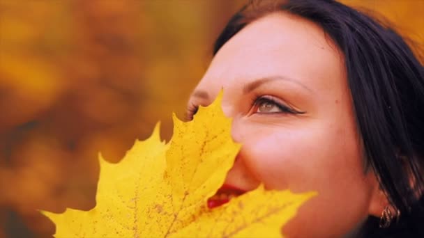 Face of a young woman with a maple leaf in the fall in the park. — Stock Video