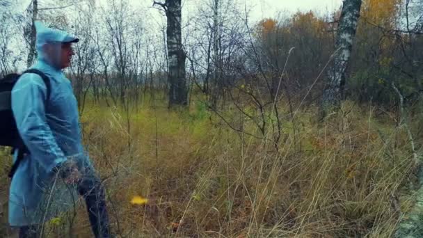 Un hombre con una mochila en un impermeable camina por el bosque y pisa un árbol caído . — Vídeos de Stock