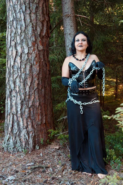 A young witch in black clothes is chained to a tree. Halloween. — Stock Photo, Image
