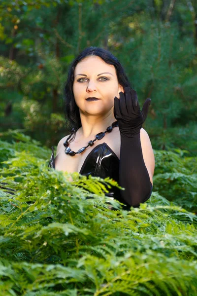 A young witch in black clothes in a forest in a thicket of fern. — Stock Photo, Image