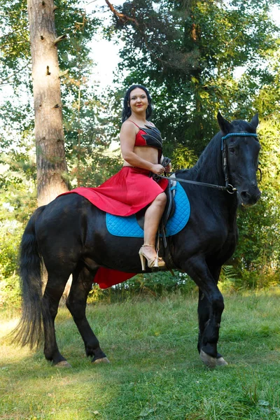 Bir at ormandaki bir eyer kırmızı elbiseli esmer genç güzel. Genel planı.