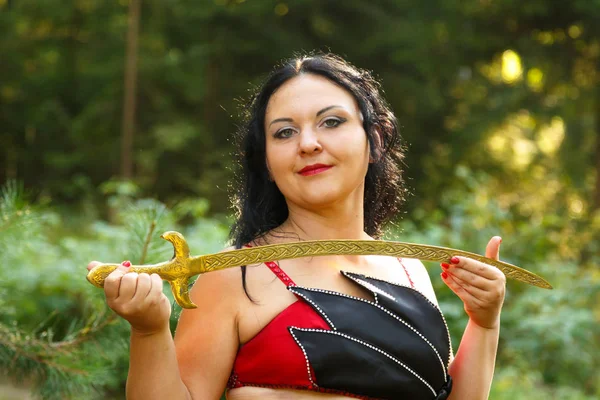 Oriental dancer in a red suit with a saber breasts on a sunny day in the forest. Close-up. — Stock Photo, Image