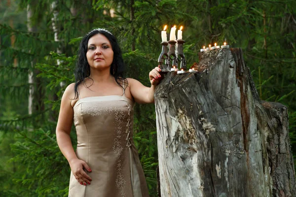 Een forest fairy in witte kleren met een kaars aangestoken kaarsen in het forest. Close-up. — Stockfoto