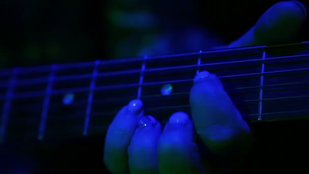 Vrouwelijke hand gaat over klemmen elektrische gitaarsnaren. Concert verlichting. Close-up. — Stockvideo