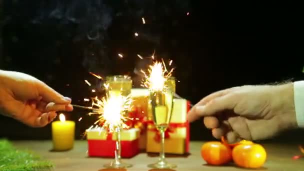 A man and a woman celebrate Christmas New Year by lighting sparklers next to their champagne glasses. — Stock Video