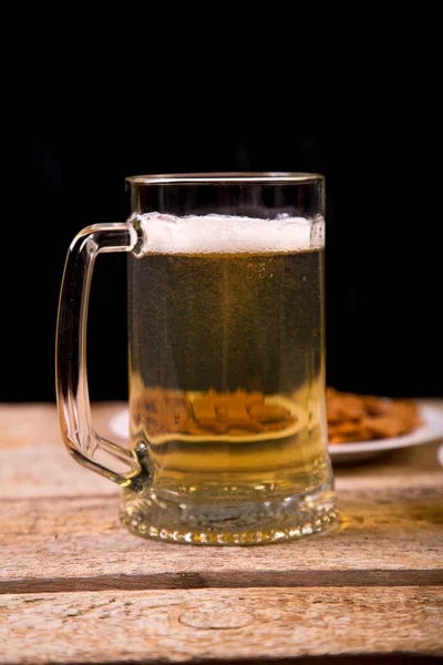 On the wooden table is a mug with a light beer. Close-up.