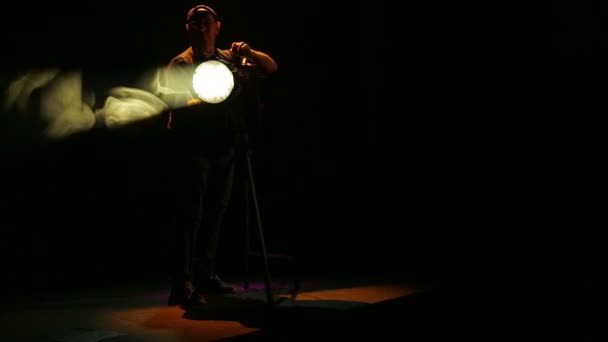 Um iluminador homem abre a abertura do projetor de perfil e dirige um feixe de luz . — Vídeo de Stock