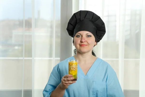 A woman cook holds a glass of fruit smoothie in her hand.