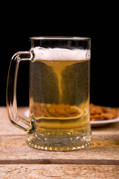 On the wooden table is a mug with a light beer.