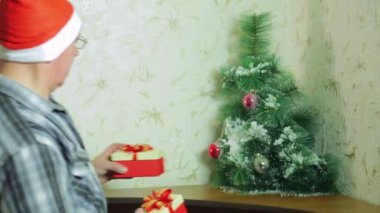 Noel Baba şapkalı bir adam Noel hediyeleri Noel ağacının altında giyiyor.