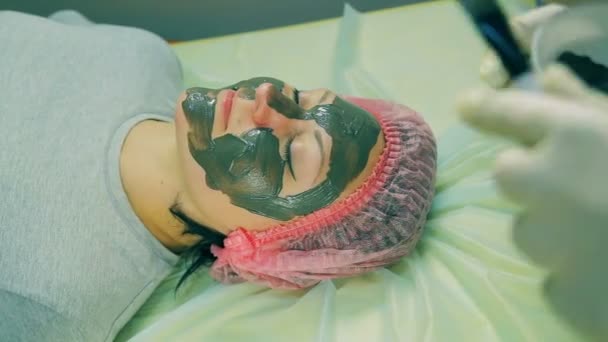 Tijd ronden. Handen van de man van de Visagist zetten op het gezicht van de vrouw een vloeibare zwart masker — Stockvideo