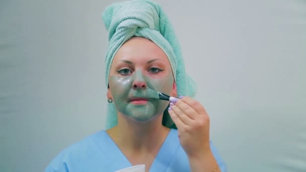 Egy fiatal nő, a fürdőszobában alkalmazza a sár maszk arcán egy kefével. Közeli kép:. — Stock videók